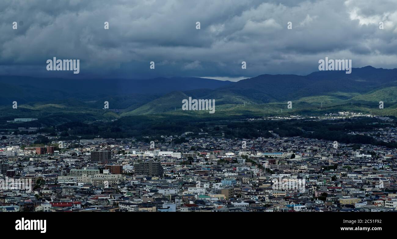 Vista diurna del bordo settentrionale della città di Hakodate, nel Giappone settentrionale, con nuvole scure e montagne boscose visibili più lontano Foto Stock