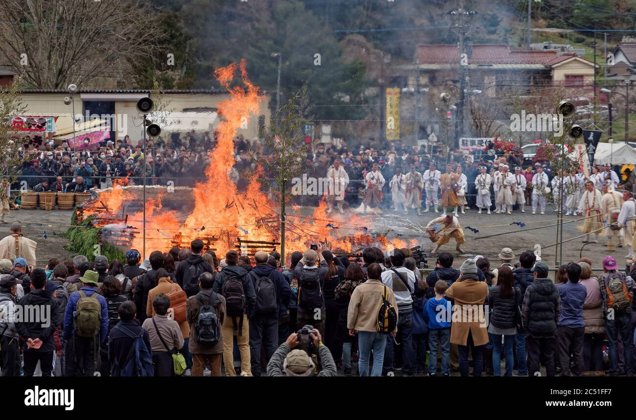 Una grande folla di orologi monaci utilizzano secchi d'acqua per controllare il falò centrale durante l'annuale festival di pompieri vicino a Mount Takao, a ovest di Tokyo Foto Stock