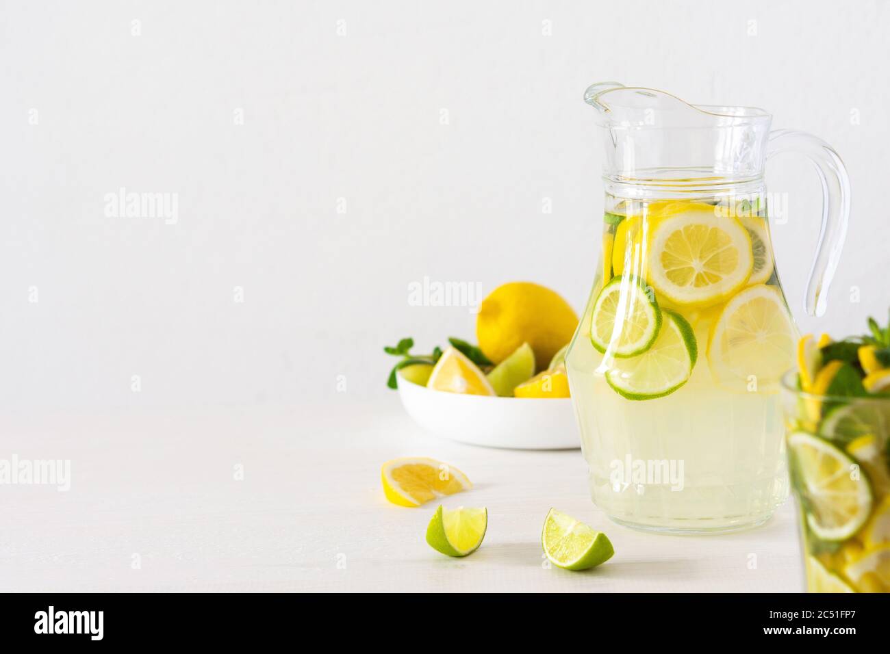 Bevanda estiva rinfrescante di limone, lime e menta, caraffa con limonata e bicchieri e fette di agrumi Foto Stock