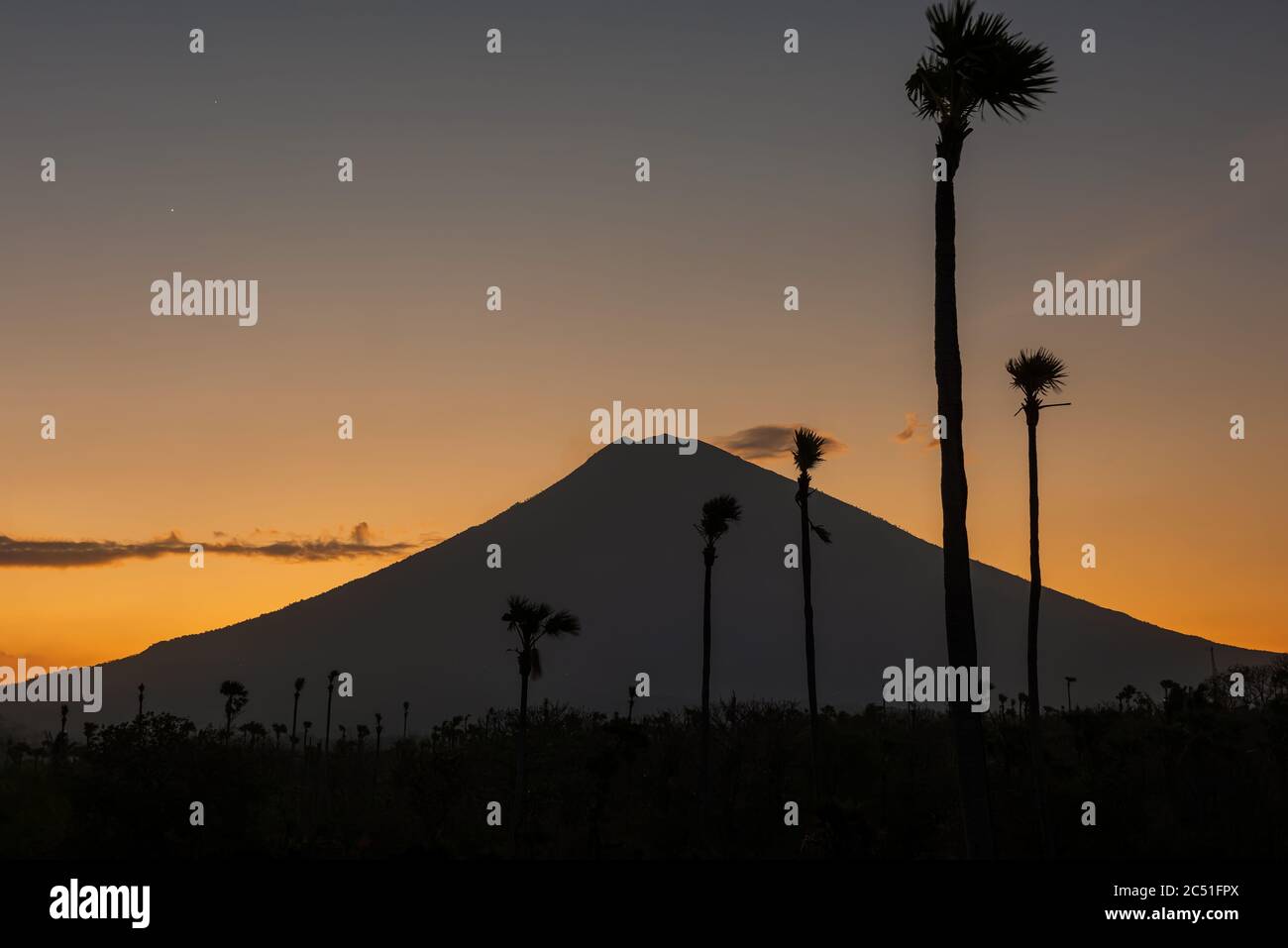 Tramonto arancione sopra il vulcano Agung, isola di Bali. Sagoma del vulcano, vista dalla spiaggia di sabbia nera al tramonto, Indonesia. Foto Stock