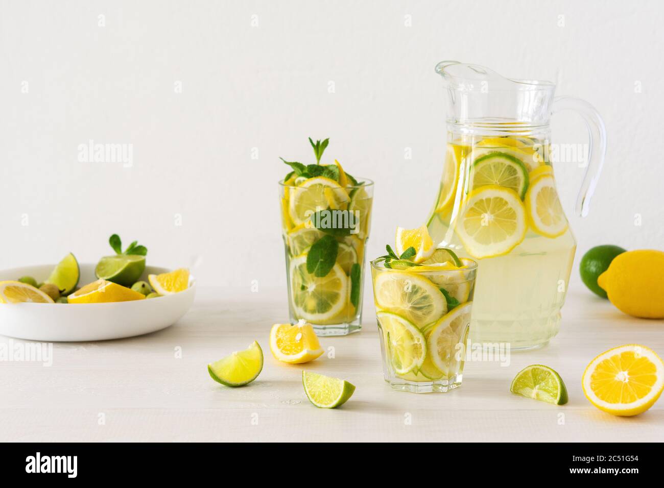 Bevanda estiva rinfrescante di limone, lime e menta, caraffa con limonata e bicchieri e fette di agrumi Foto Stock