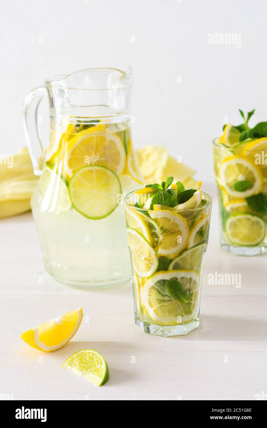 Bevanda estiva rinfrescante di limone, lime e menta, caraffa con limonata e bicchieri e fette di agrumi Foto Stock