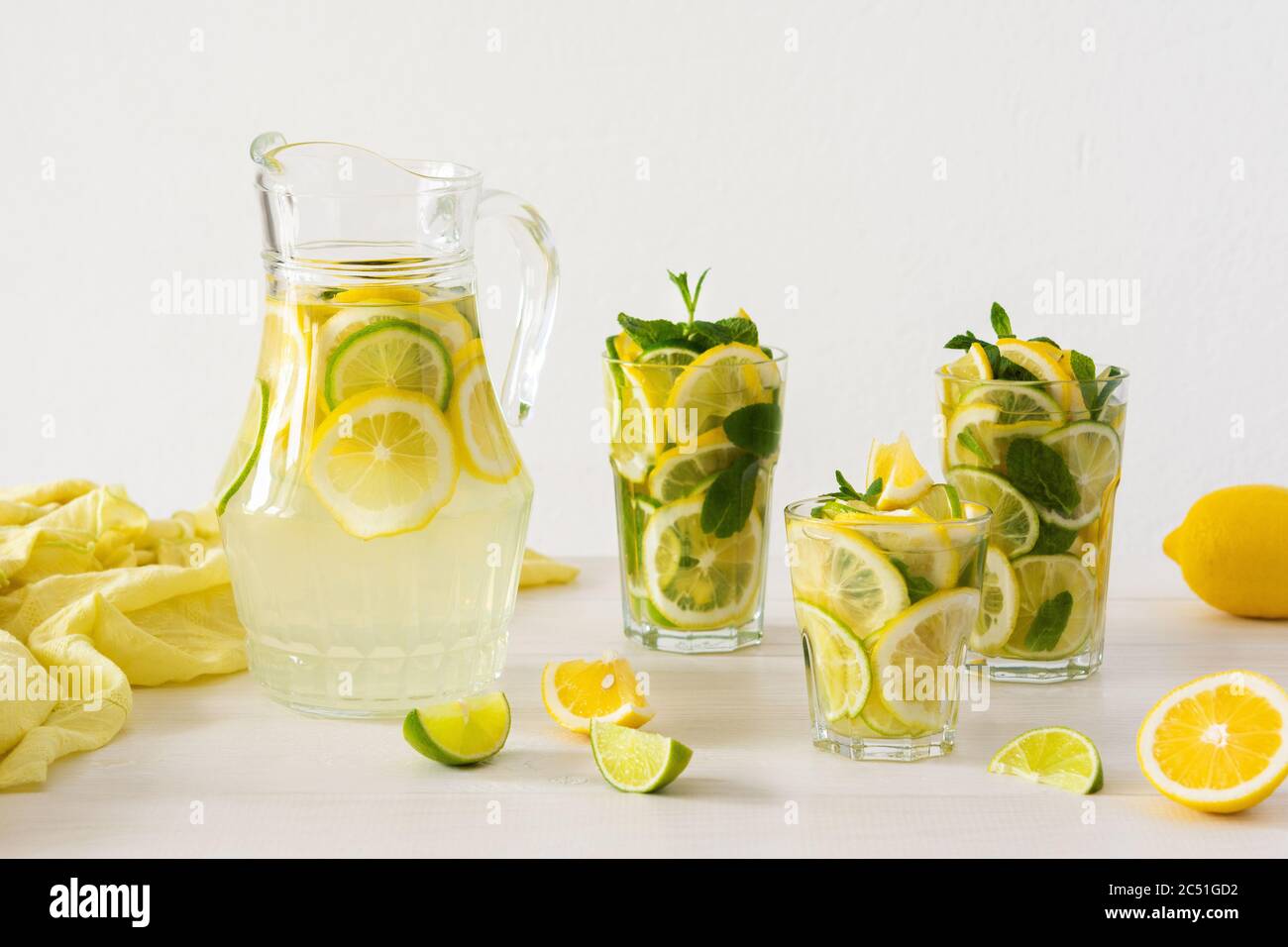 Bevanda estiva rinfrescante di limone, lime e menta, caraffa con limonata e bicchieri e fette di agrumi Foto Stock