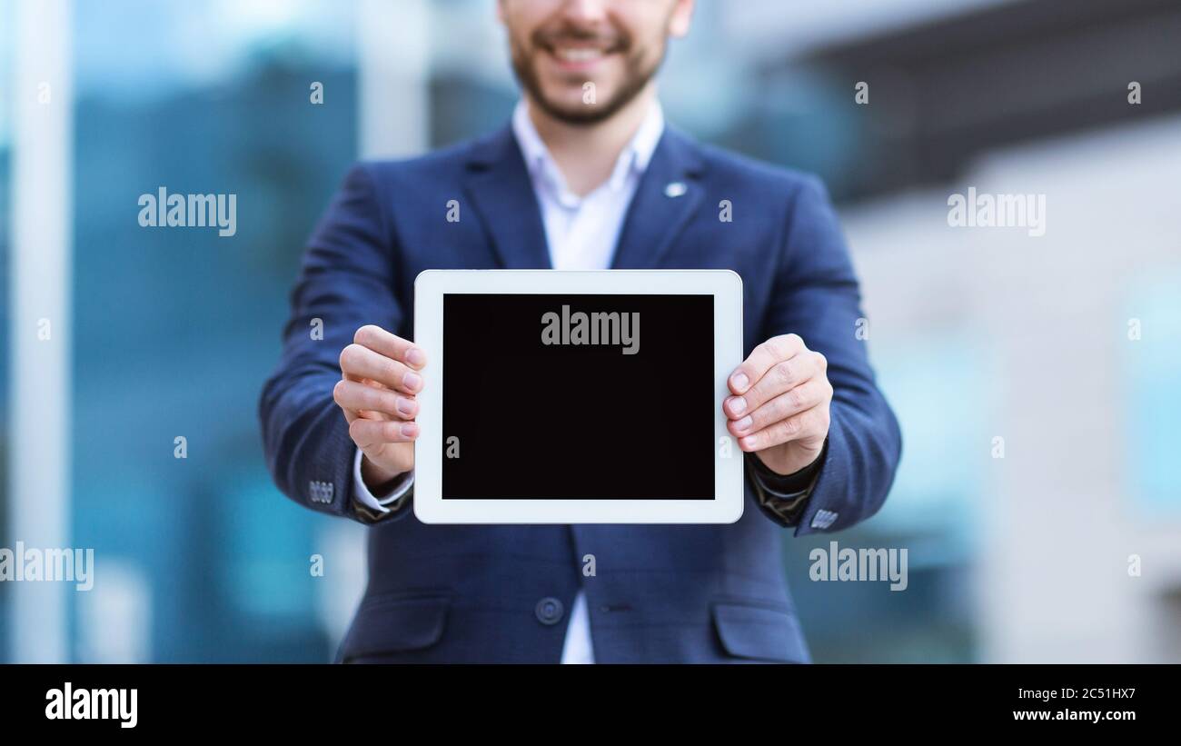 Vista in primo piano di un giovane uomo d'affari che mostra un computer tablet con schermo vuoto sulla strada della città, mockup per il tuo design Foto Stock