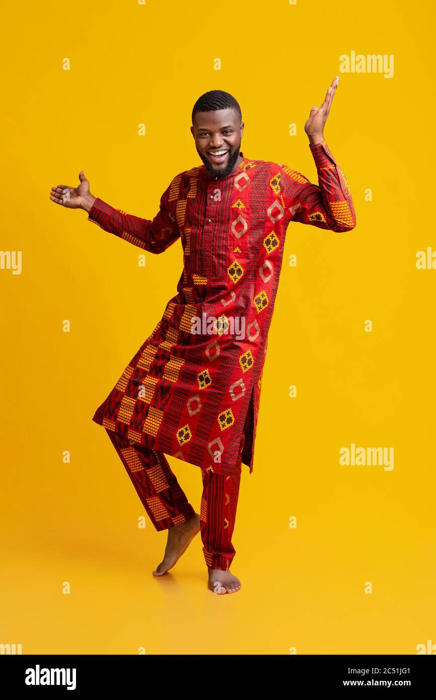 Uomo africano positivo in abito tradizionale danzante sopra il giallo Foto Stock