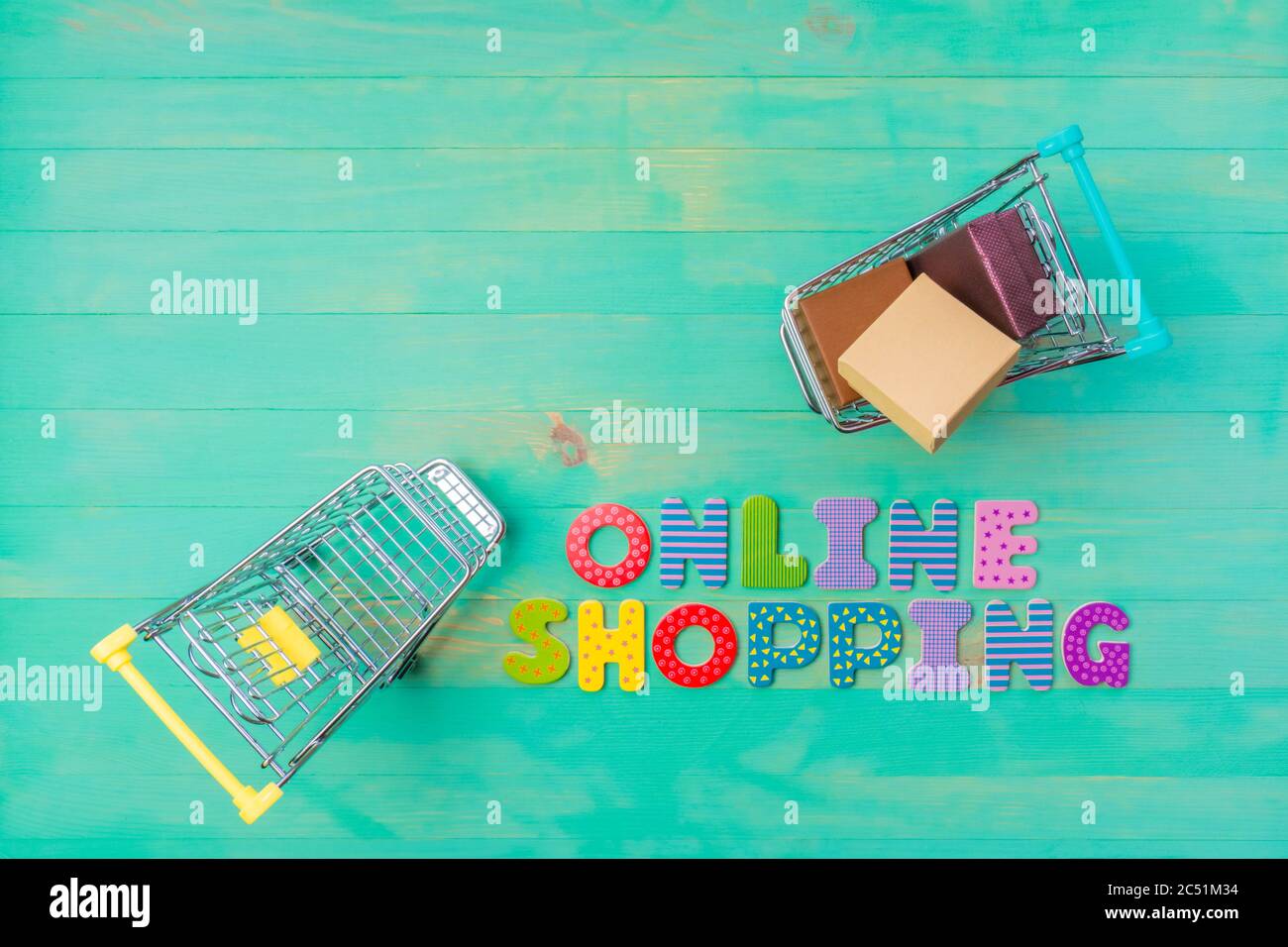 Carrelli vuoti e pieni e parole SHOPPING ONLINE su sfondo di legno verde. Vista dall'alto di negozi online di parole e due carrelli e spazio per fotocopie. IO Foto Stock