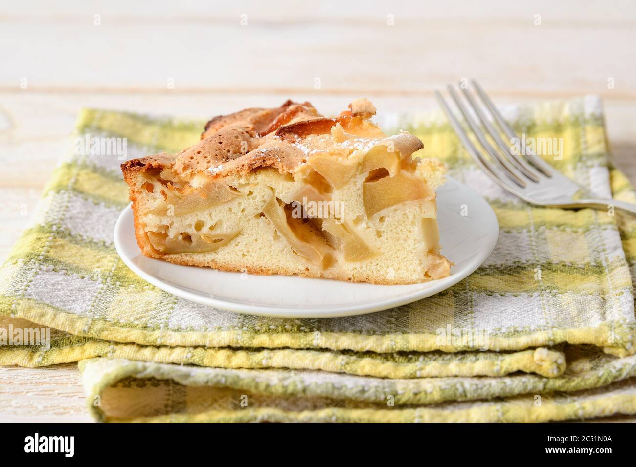 Un pezzo grande di torta di mele dolce e acide su un piatto bianco su un tovagliolo giallo-verde a scacchi. Ricetta per dolci e dolci fatti in casa. Pasticceria per la colazione. Foto Stock