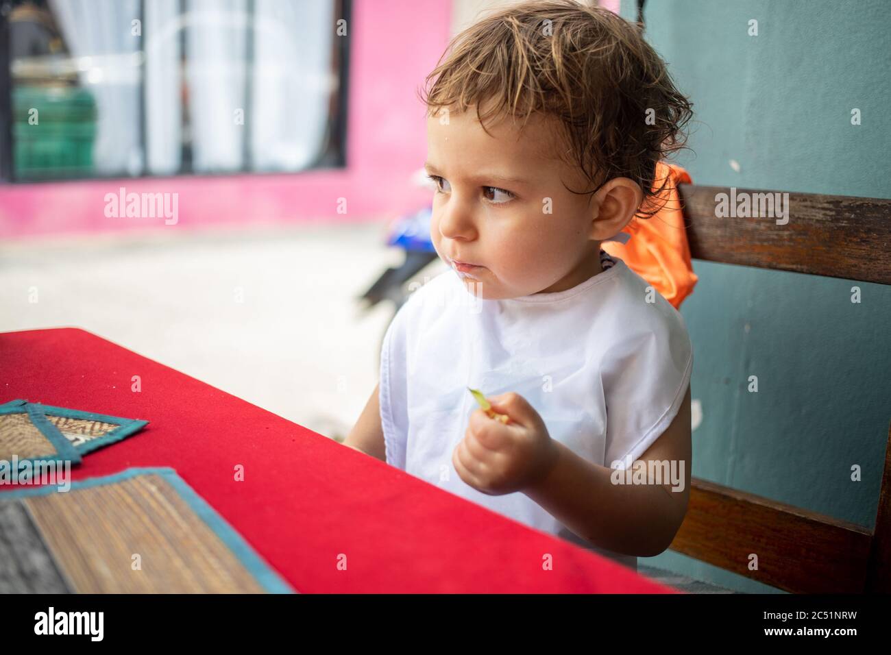 carino bambino piccolo in bib pensato mentre provava il cibo seduto ad un tavolo su una terrazza di caffè di strada Foto Stock
