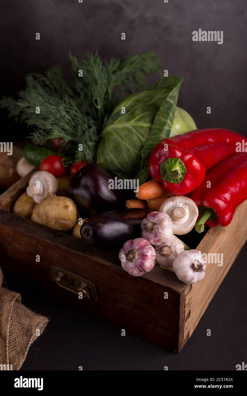 Assortimento di verdure fresche crude in una scatola di legno su sfondo nero. Cibo locale biologico sano. Foto Stock