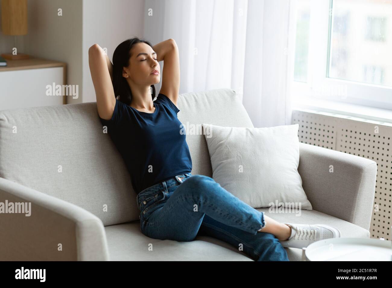 Donna pacifica rilassante con gli occhi chiusi seduta sul divano interno Foto Stock
