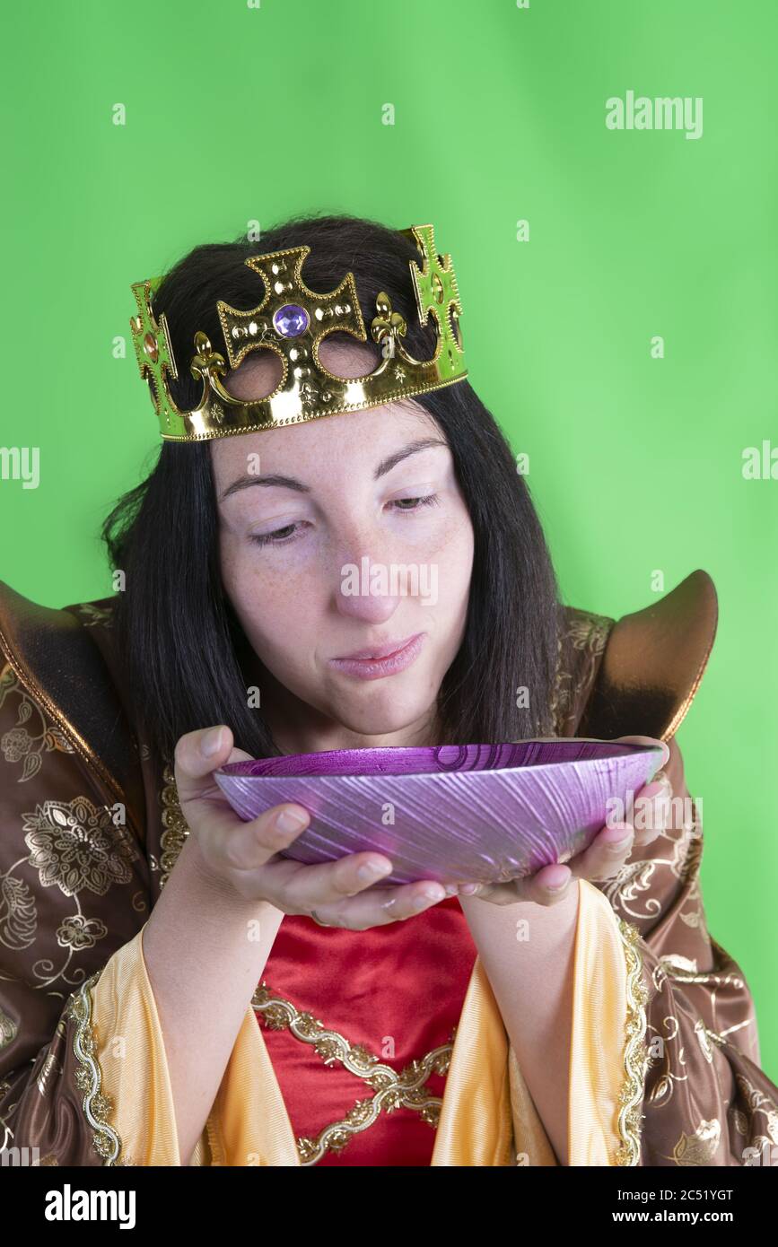 Primo piano di una femmina caucasica in costume oro medievale e. una corona in posa con una ciotola viola Foto Stock