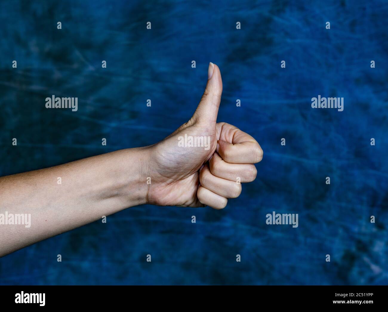 Immagine orizzontale di una mano bianca che mostra i pollici su un sfondo blu marmorizzato Foto Stock
