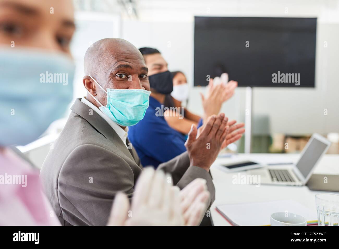 Gli uomini d'affari con maschera donano applausi in un seminario sulla comunicazione video Foto Stock