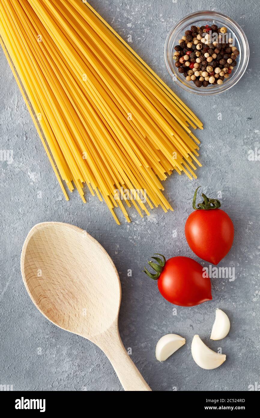Spaghetti crudi con pomodori, aglio, pepe e cucchiaio di legno su fondo grigio. Vista dall'alto. Foto Stock