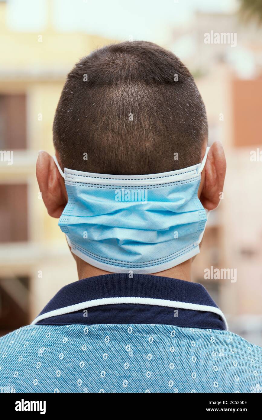 primo piano di un uomo per strada, in abbigliamento casual, indossando la sua maschera chirurgica nella parte posteriore del collo mentre non lo indossa in faccia Foto Stock