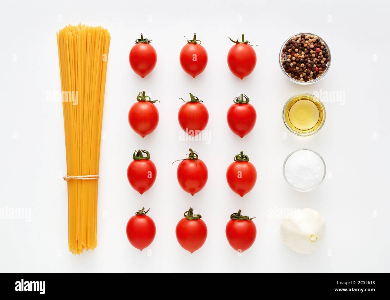 Spaghetti crudi con pomodori, aglio, pepe, sale e olio d'oliva su fondo bianco. Preparazione della pasta e ricetta della salsa. Foto Stock