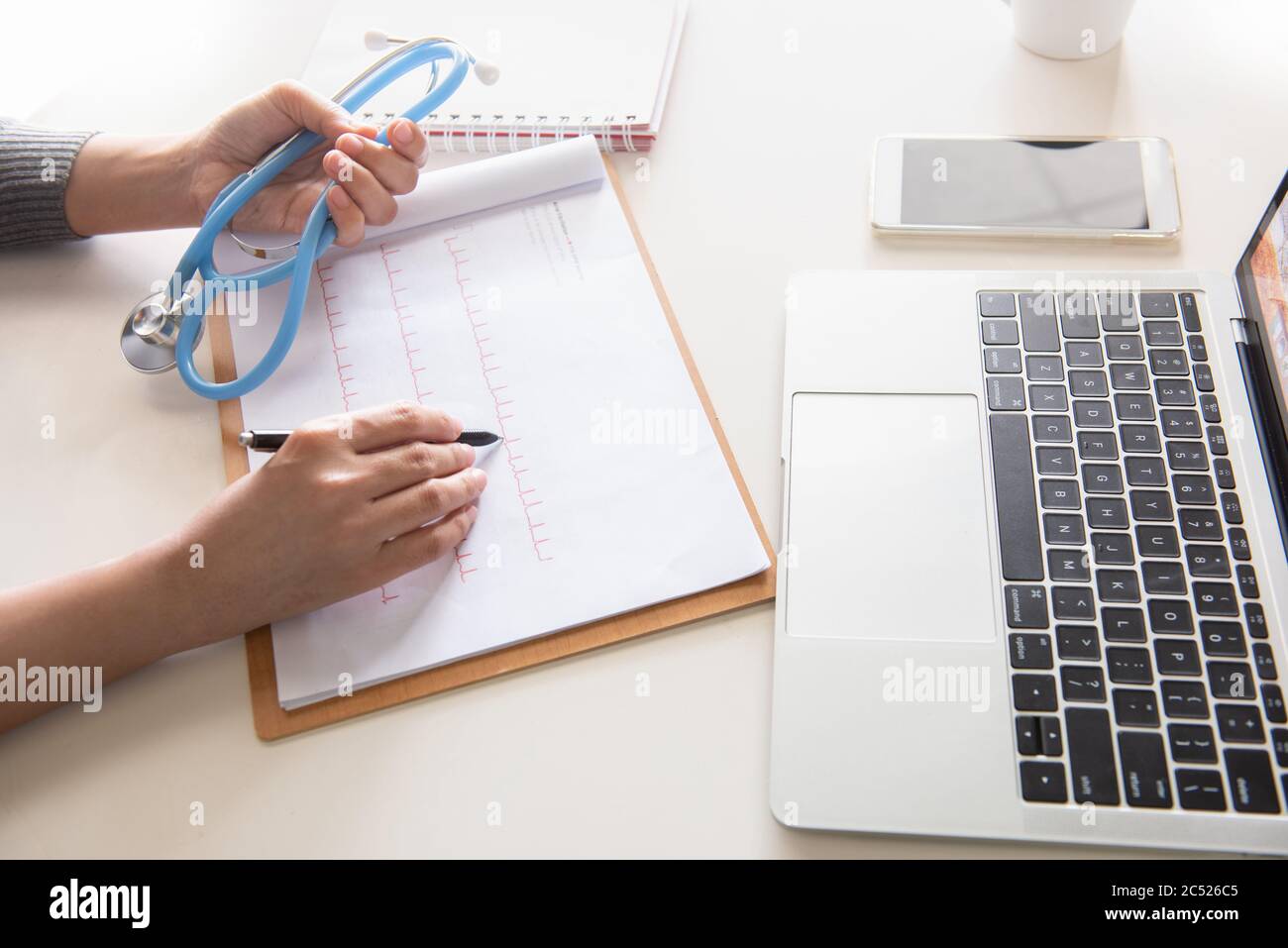 Primo piano di mani del medico che scrivono prescrizione e stetoscopio di tenuta in moderno ufficio in ospedale. Concetto sanitario e medico. Foto Stock