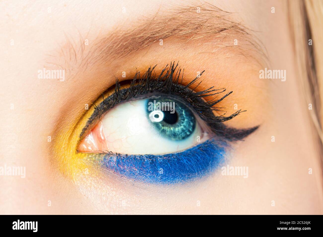 Occhio donna che guarda in su. L'ombretto blu e giallo e la freccia nera del palpebre costituiscono un primo piano Foto Stock