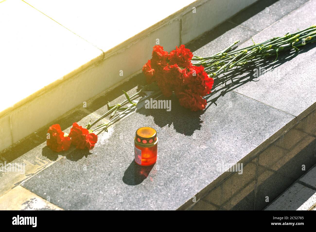 Garofani rossi su una lastra di marmo. Fiori sul monumento e una lampada. Simbolo di lutto. Foto Stock