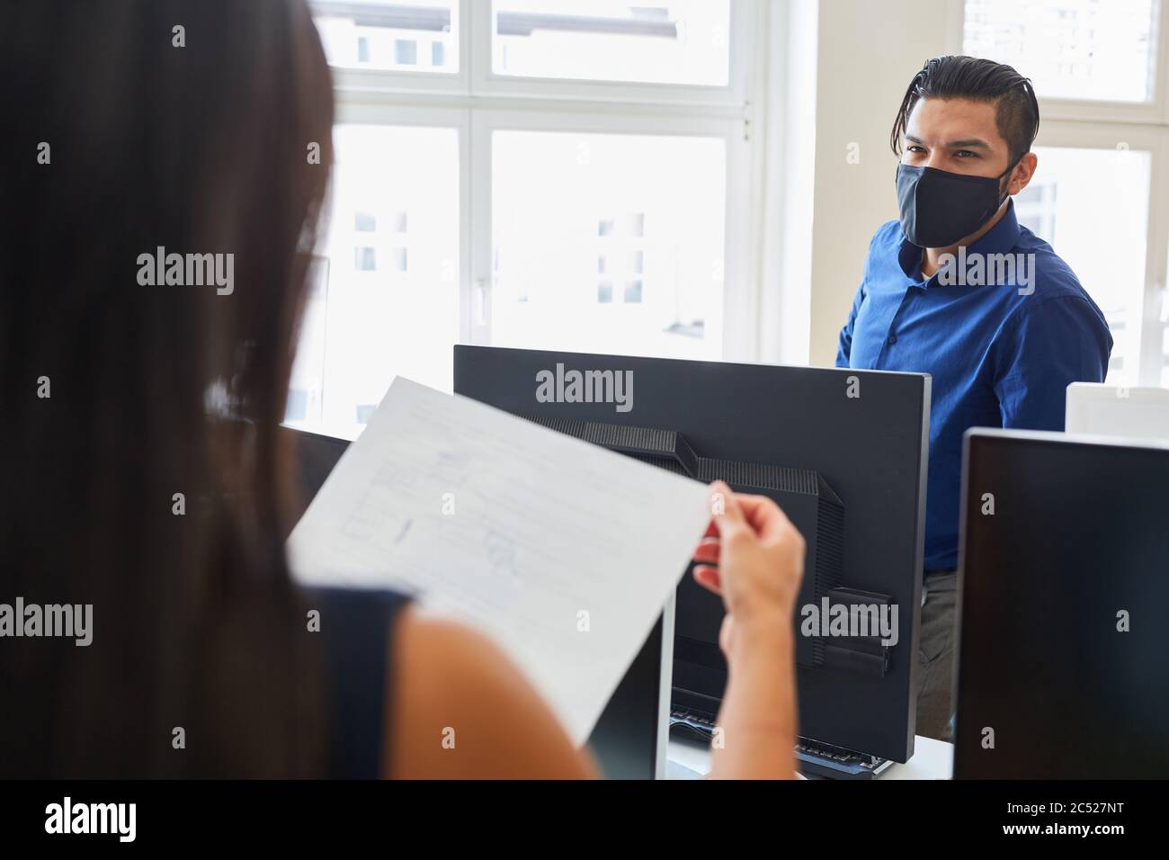 Due uomini d'affari con protezione bocca-naso lavorano insieme in ufficio Foto Stock