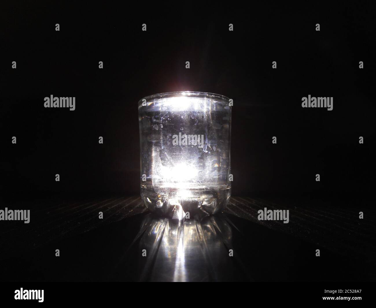 vetro dell'acqua sul tavolo, sullo sfondo come luce del flash, nero. Foto Stock