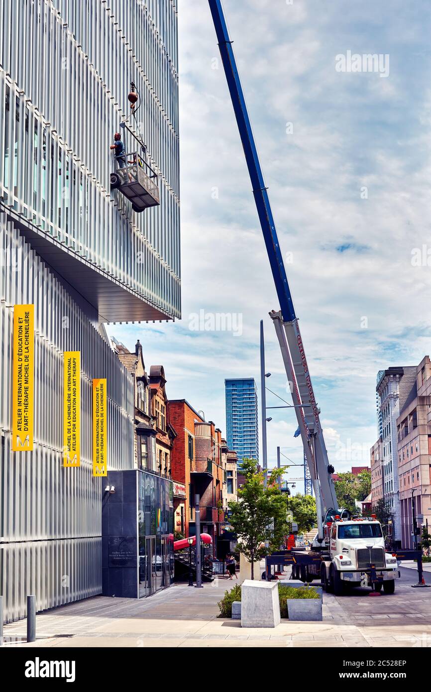 Montreal, Canada - Giugno, 2018: Una gru e lavoratori su una piattaforma di ascensore che puliscono le finestre di un edificio sulla via del vescovo a Montreal, Quebec, Canada. Foto Stock