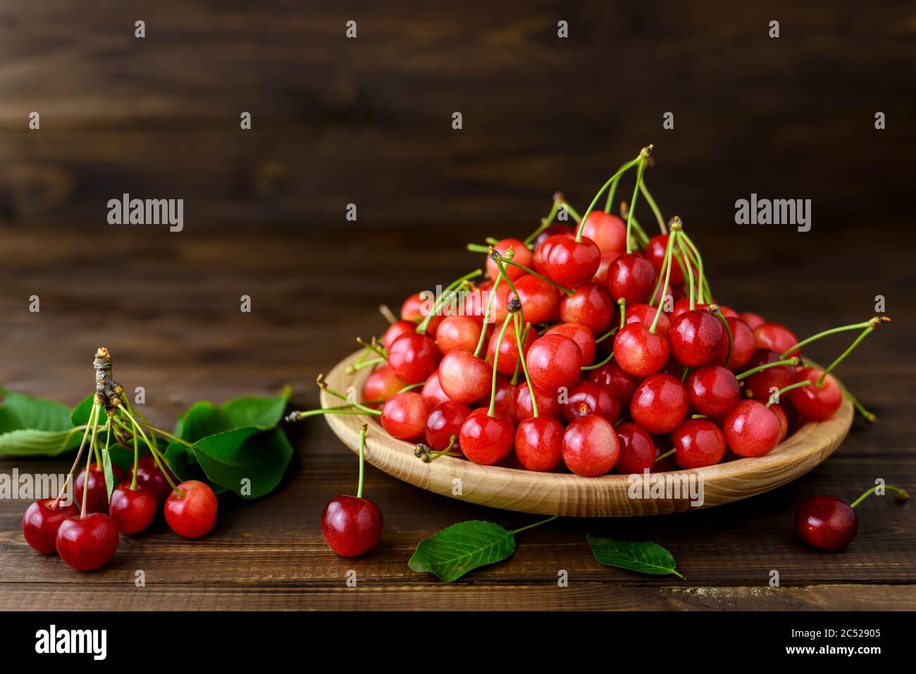 Ciliegie rosse dolci in un piatto di legno e foglie verdi su un tavolo di legno marrone con spazio per la copia del testo. Foto Stock