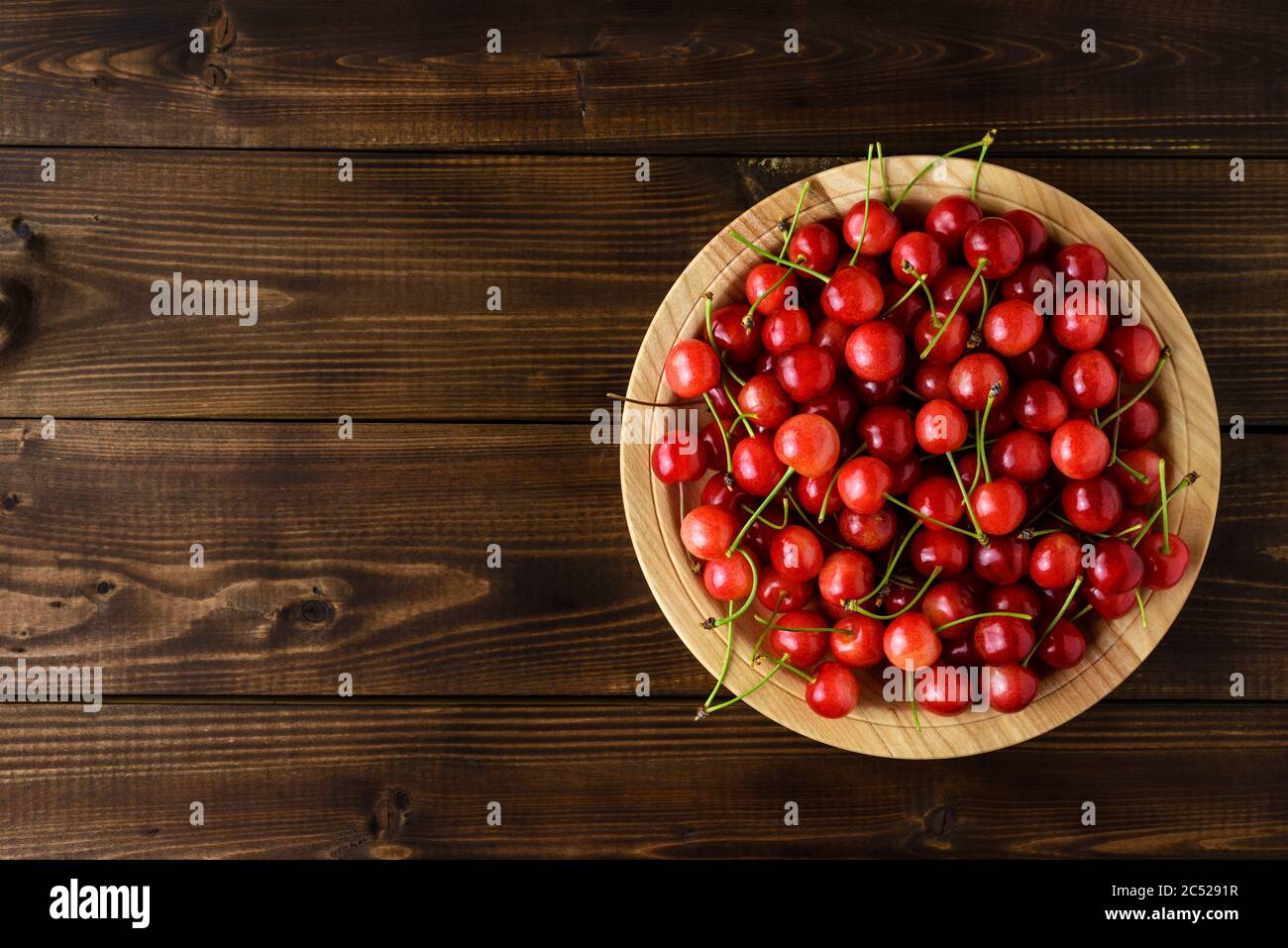Ciliegie rosse dolci in una ciotola di legno su un tavolo di legno marrone con spazio per la copia del testo. Vista dall'alto. Foto Stock