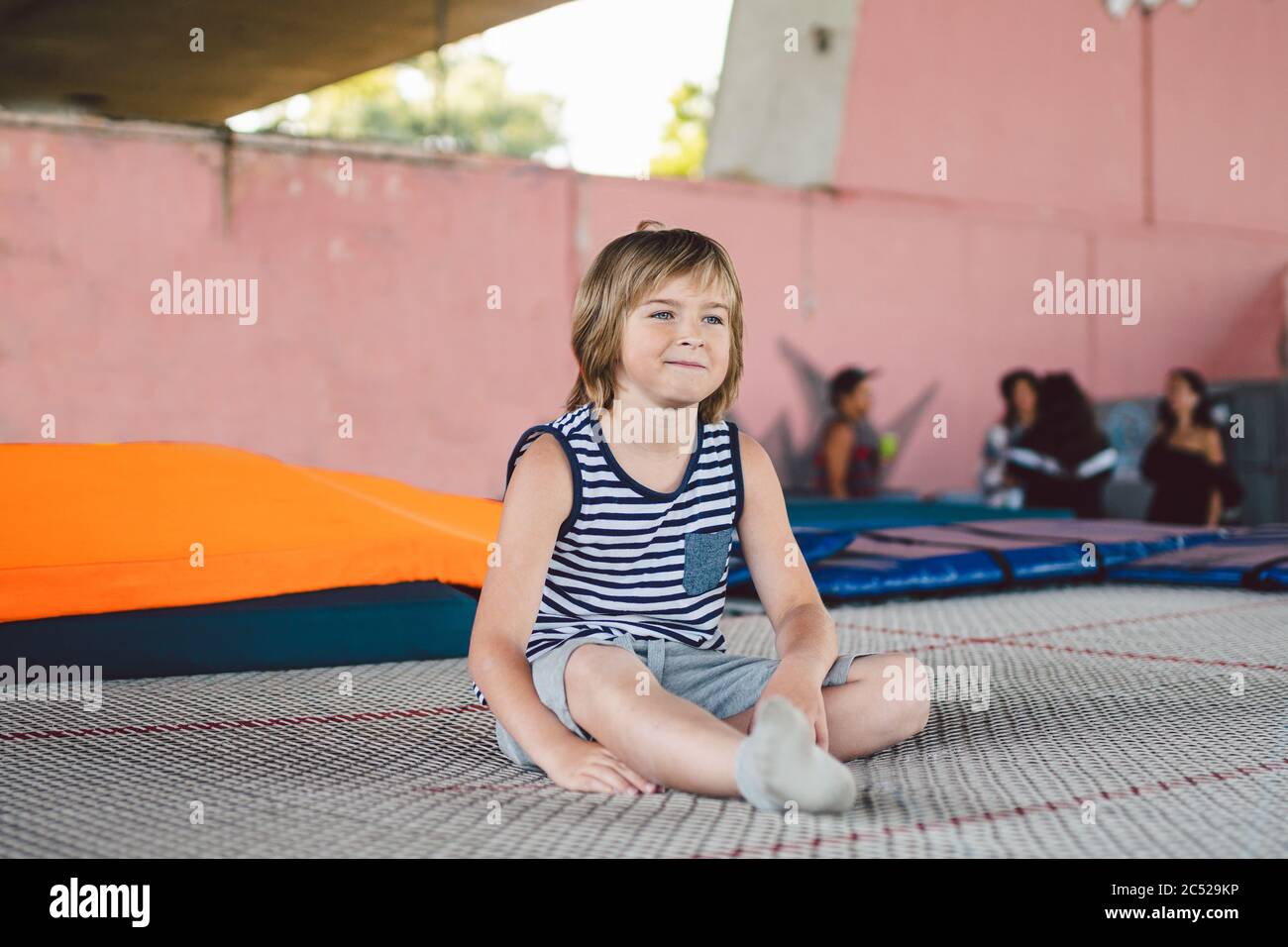 Atleta caucasico ragazzo seduto sul trampolino dopo l'allenamento. Bambino è impegnato in trampolino professionale all'esterno. Piccolo ragazzo Foto Stock