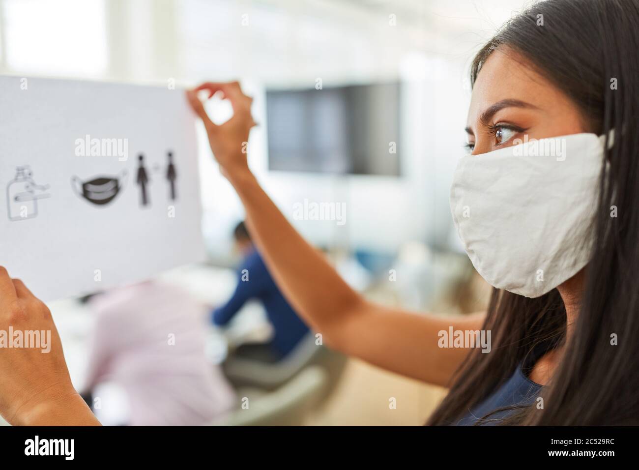 Donna d'affari con maschera a causa di Covid-19 fastens una scheda di notifica con regole igieniche in ufficio Foto Stock