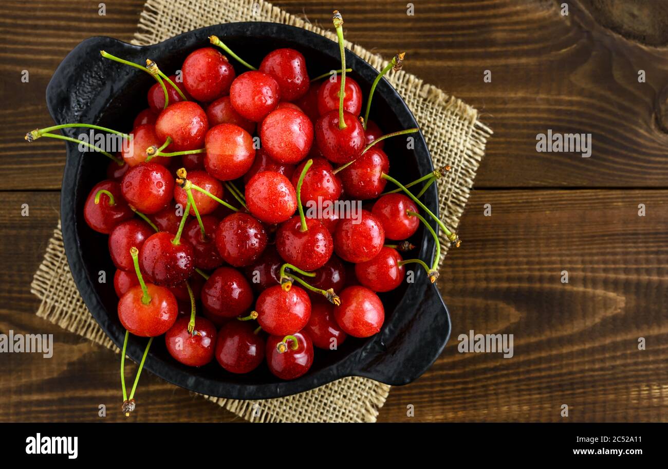 Ciliegie rosse dolci in una ciotola nera su un tavolo di legno marrone con spazio per la copia del testo. Vista dall'alto. Foto Stock