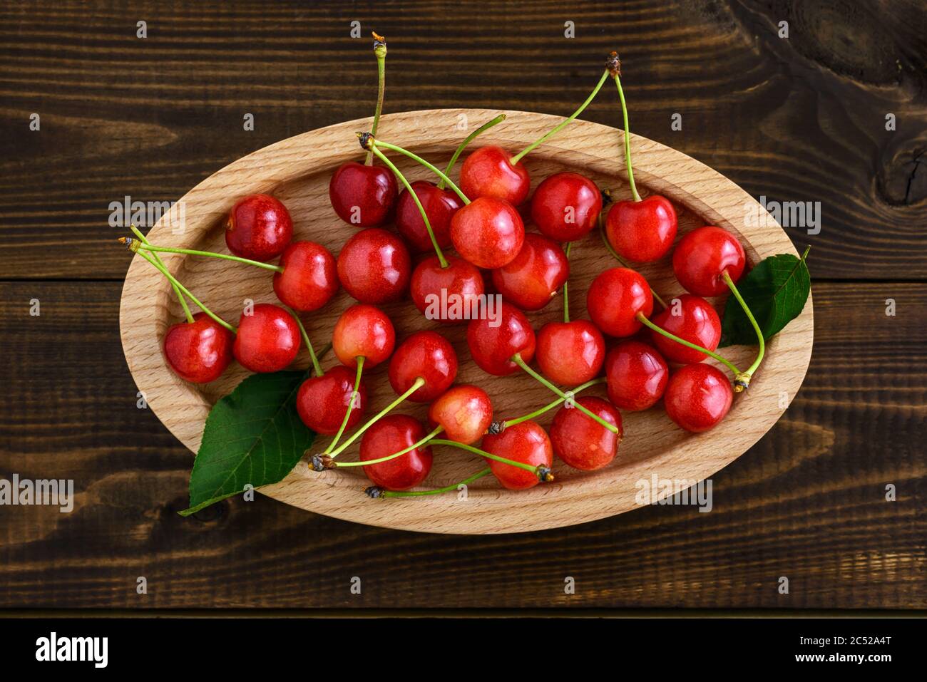 Ciliegie rosse dolci in una ciotola ovale di legno su un tavolo di legno marrone. Vista dall'alto. Foto Stock
