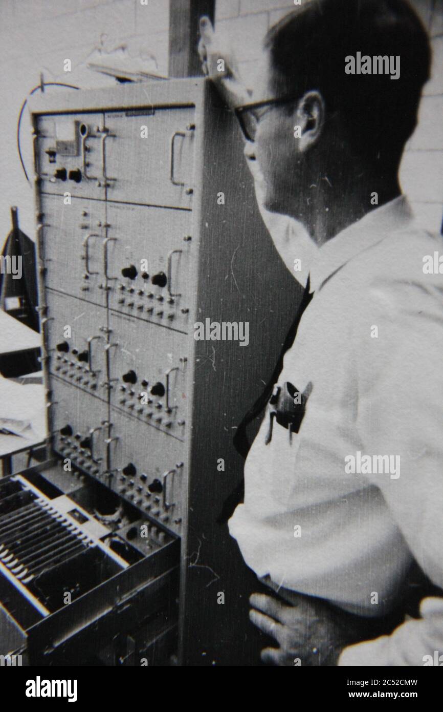 Fine anni '70 vintage nero e bianco stile di vita fotografia di un uomo professionale che gestisce un super computer in ufficio. Foto Stock