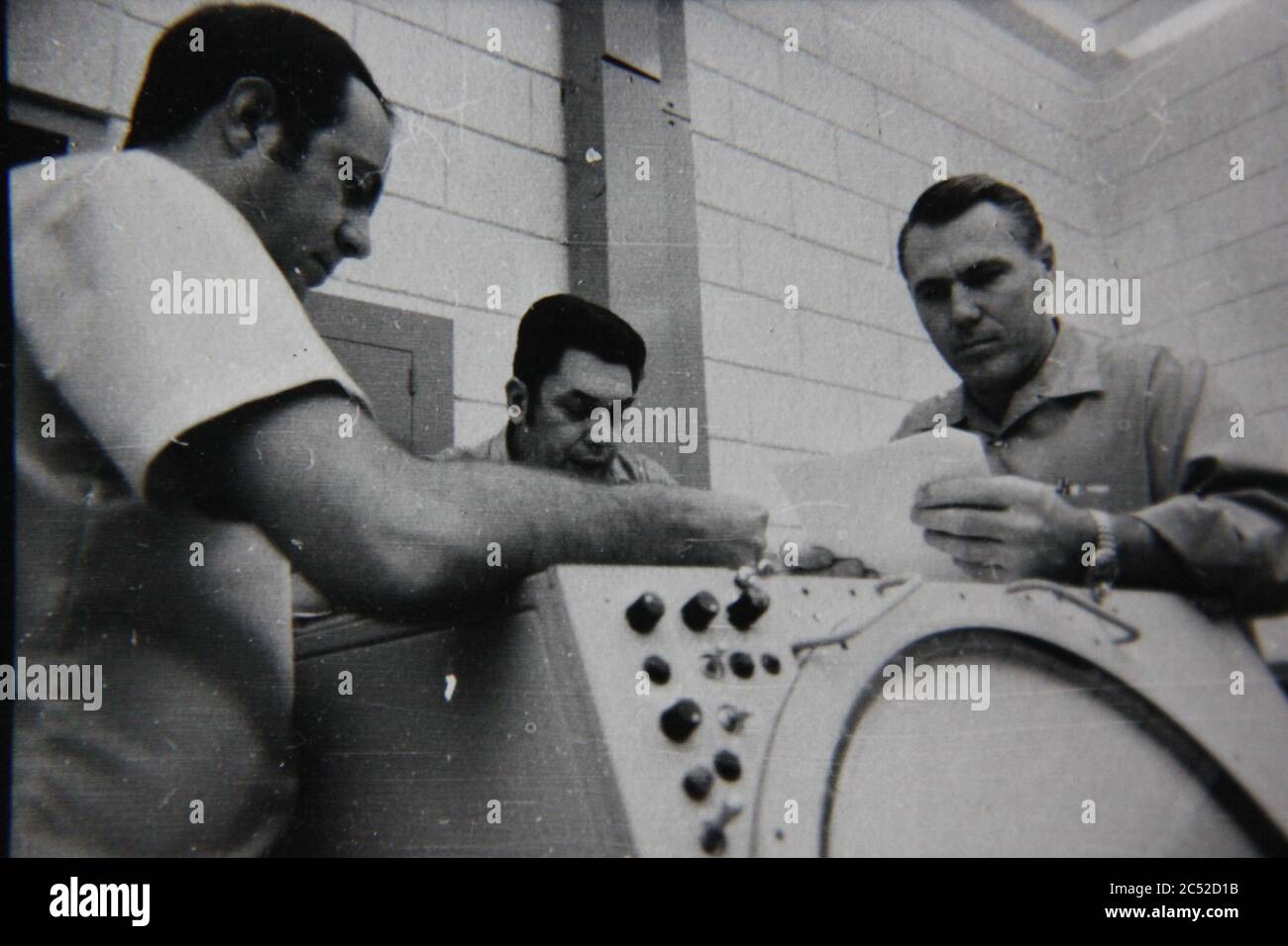 Fine anni 70 vintage nero e bianco stile di vita fotografia di tre uomini che parlano di un radar super computer assembly. Foto Stock
