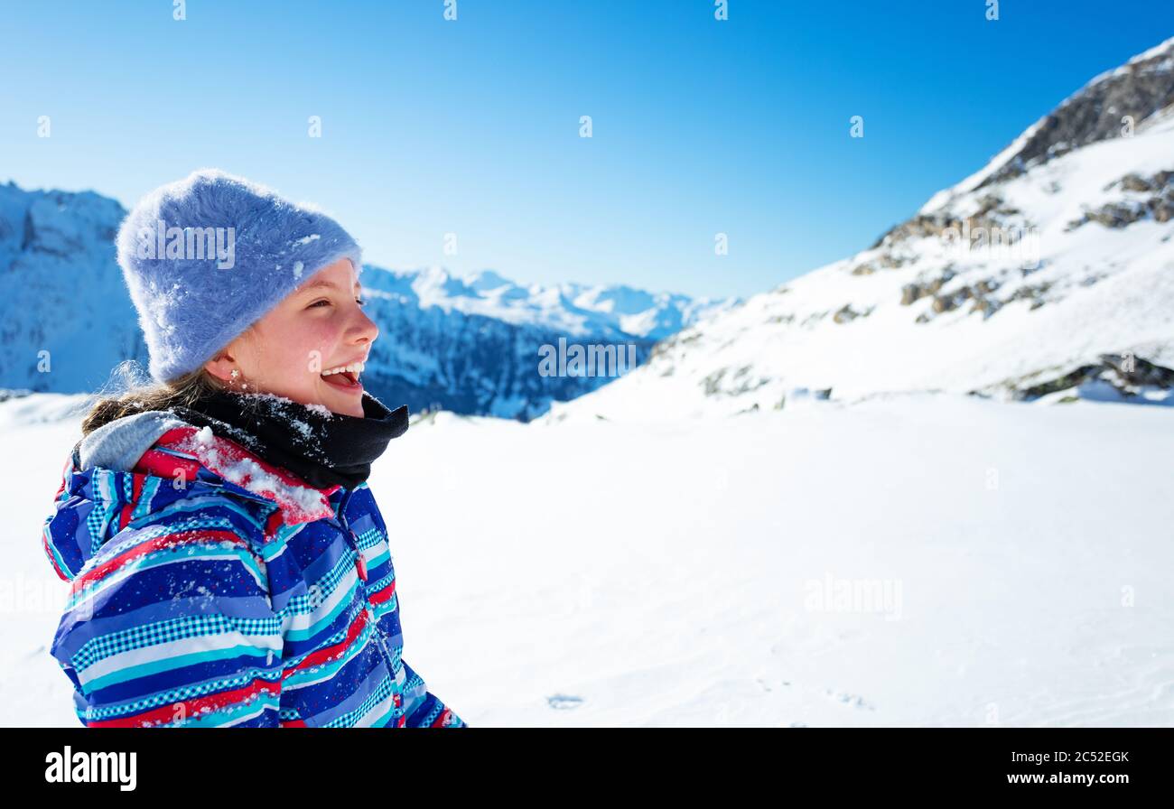 Felice ridere con ragazza a bocca aperta in cappello da sci e cappotto colore alto in neve coperta vista montagne nel profilo Foto Stock