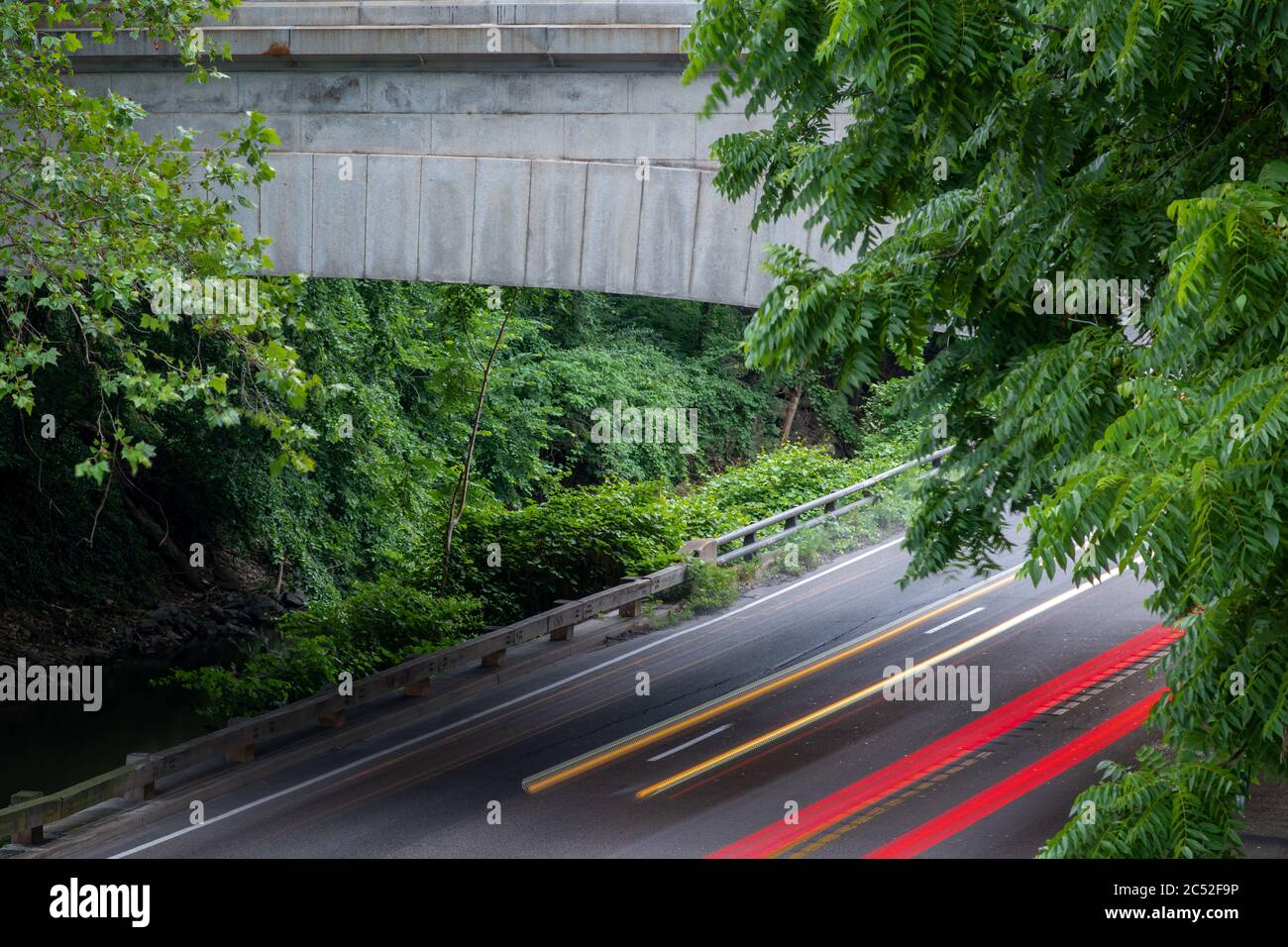 Lunga esposizione foto di ponte in cemento in un'area boscosa con striature di luce gialla e rossa da auto veloci sulla strada. Foto Stock