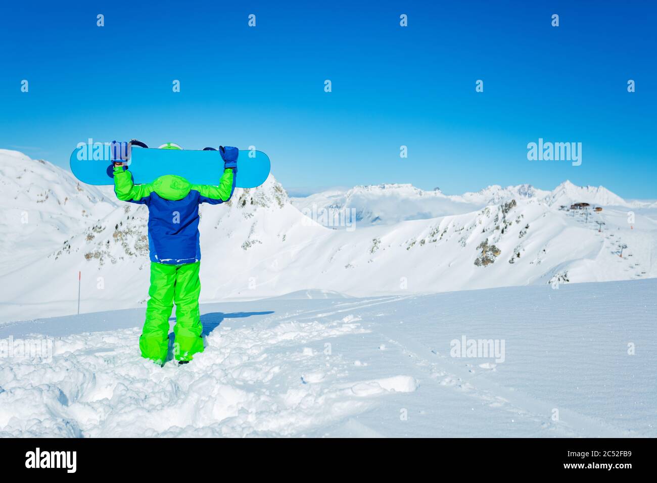Vista da dietro di un supporto per ragazzi tenere lo snowboard sopra la testa in mani sulla neve in maschera, casco da sci Foto Stock