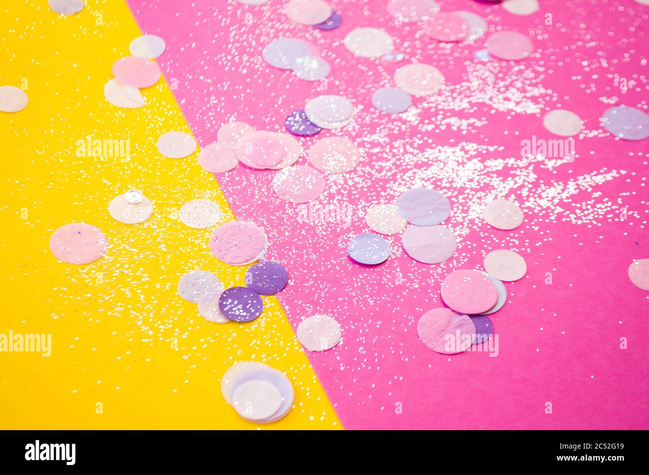 Confetti colorati, scintillano su sfondo rosa e giallo brillante. Sfondo festivo. Foto Stock