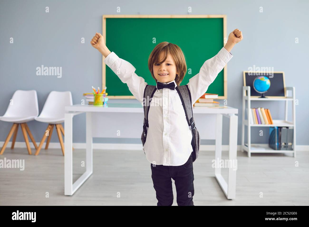 Ritorno a scuola. Divertente scolaro con zaino alzò le mani in piedi in classe. Foto Stock
