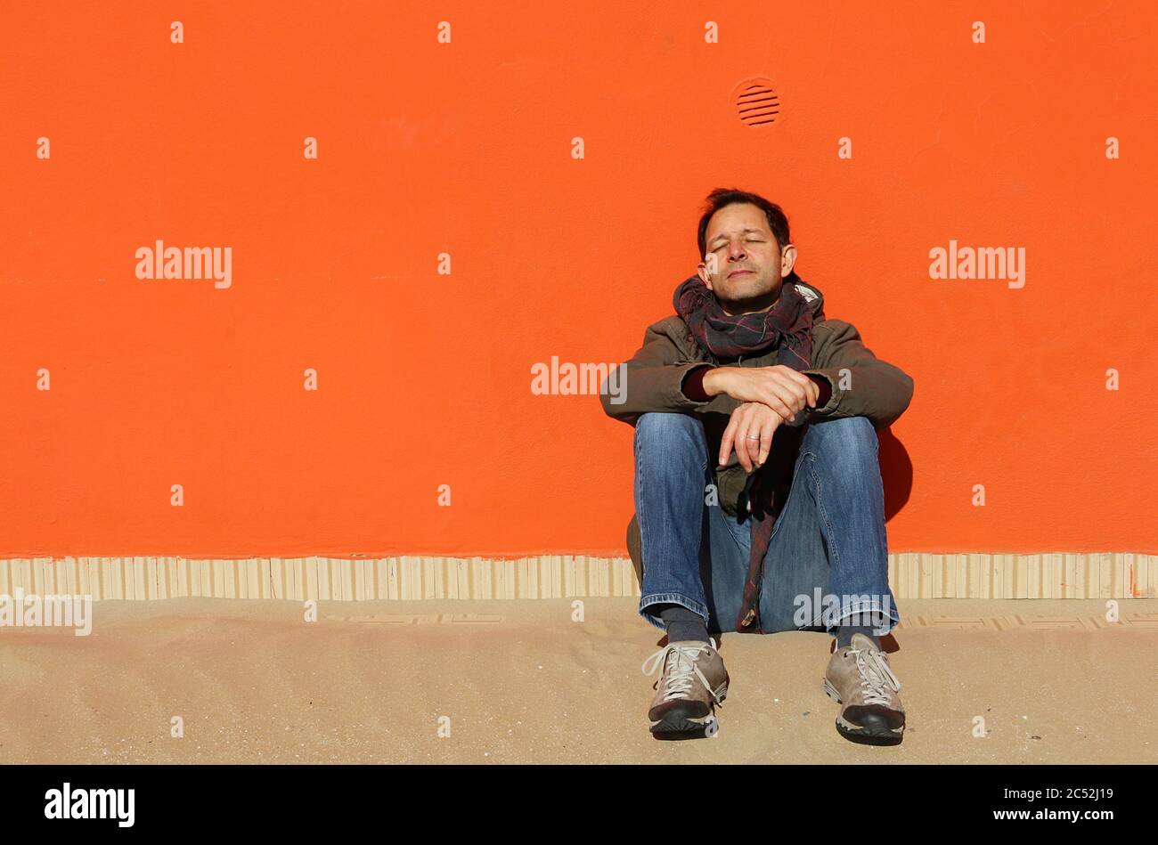 Ritratto di uomo seduto sulla spiaggia appoggiato a una parete arancione al sole, Rimini, Emilia-Romagna, Italia Foto Stock