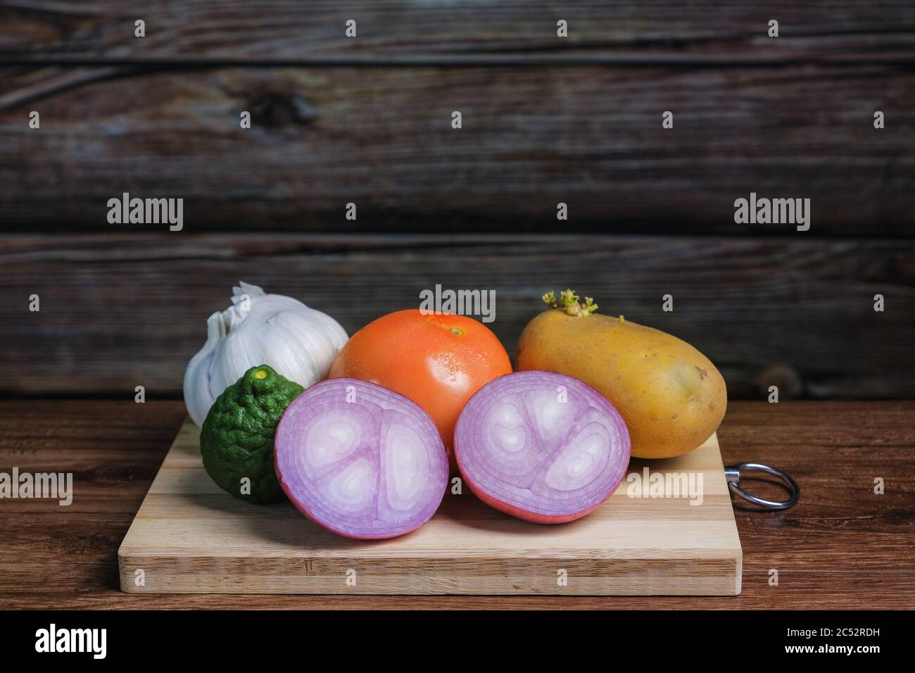 Pomodoro, aglio, lime kaffir, cipolla e patate su un tagliere di legno Foto Stock