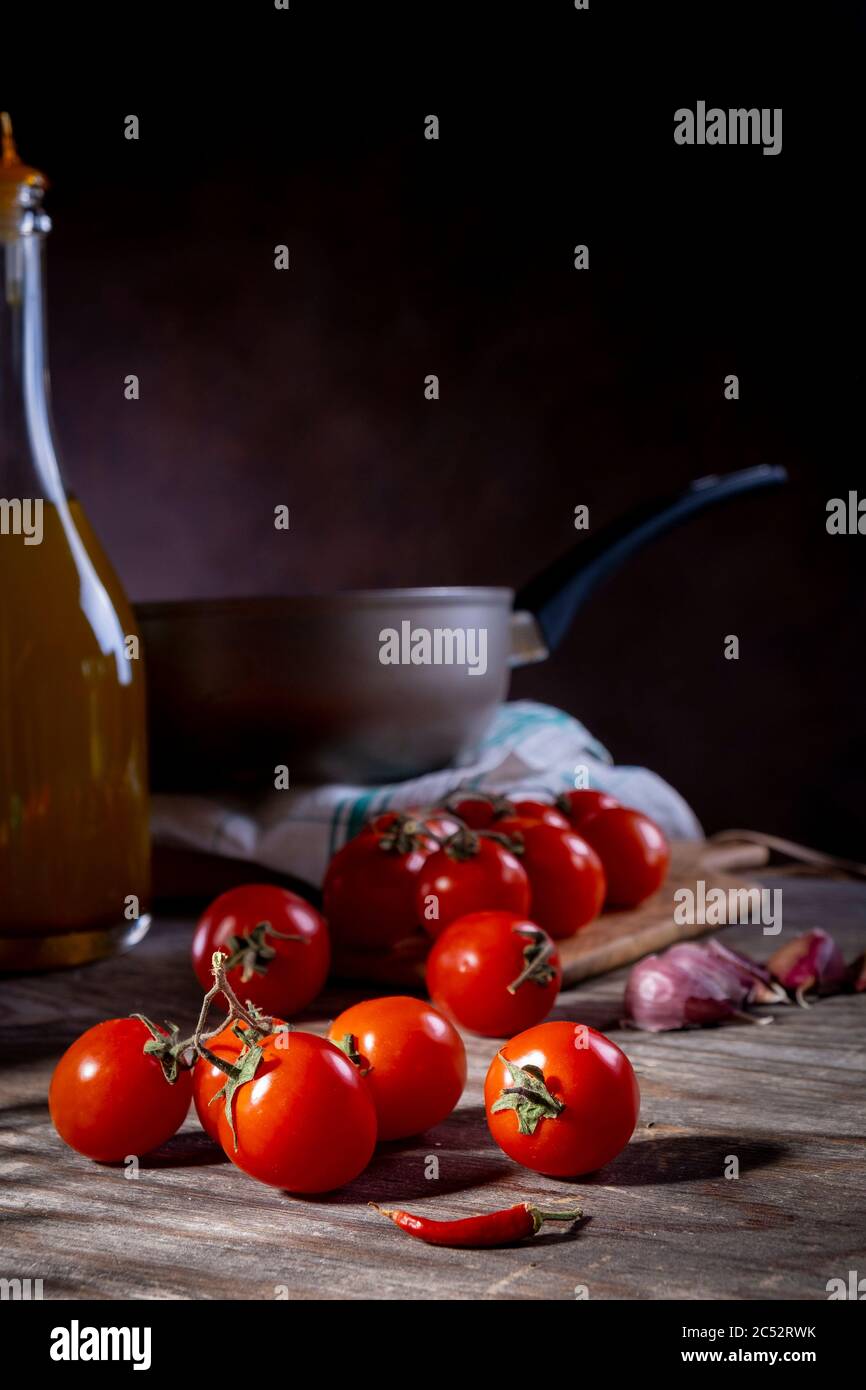 Pomodori ciliegini su tavolo di legno vecchio con aglio, peperoncino e olio d'oliva Foto Stock