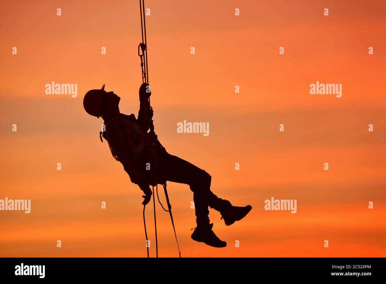 Silhouette di un lavoratore di costruzione appeso su un'imbracatura di sicurezza in un cantiere, Thailandia Foto Stock