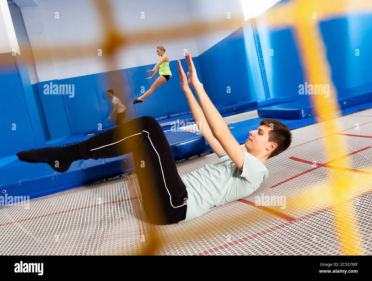 Vista attraverso la rete di sicurezza gialla di jumps di allenamento maschile adolescente ginnastica su trampolino allenamento Foto Stock