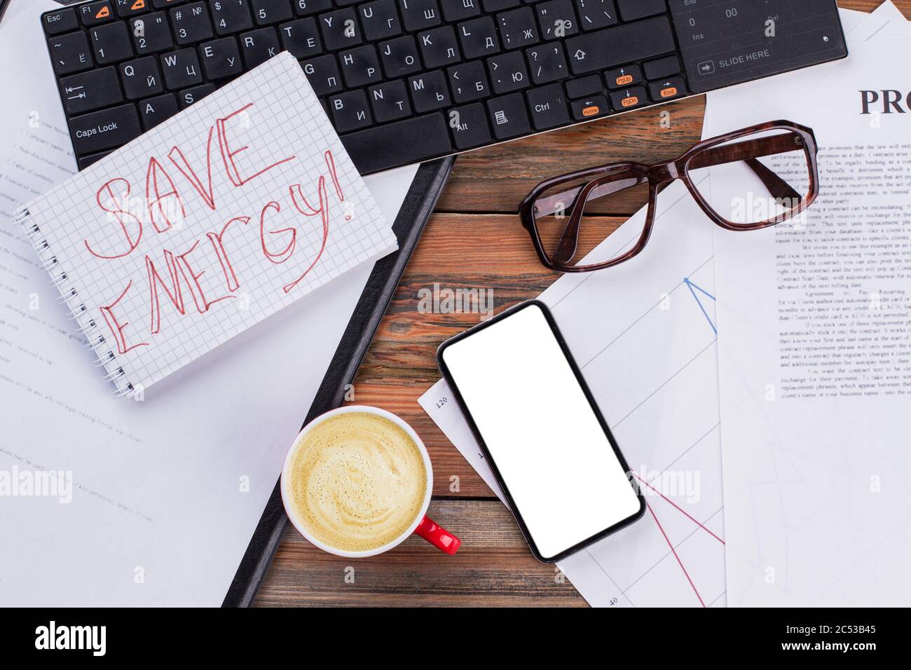 Scrivania moderna con smartphone con schermo nero, notebook, bicchieri e tazza di caffè. Foto Stock