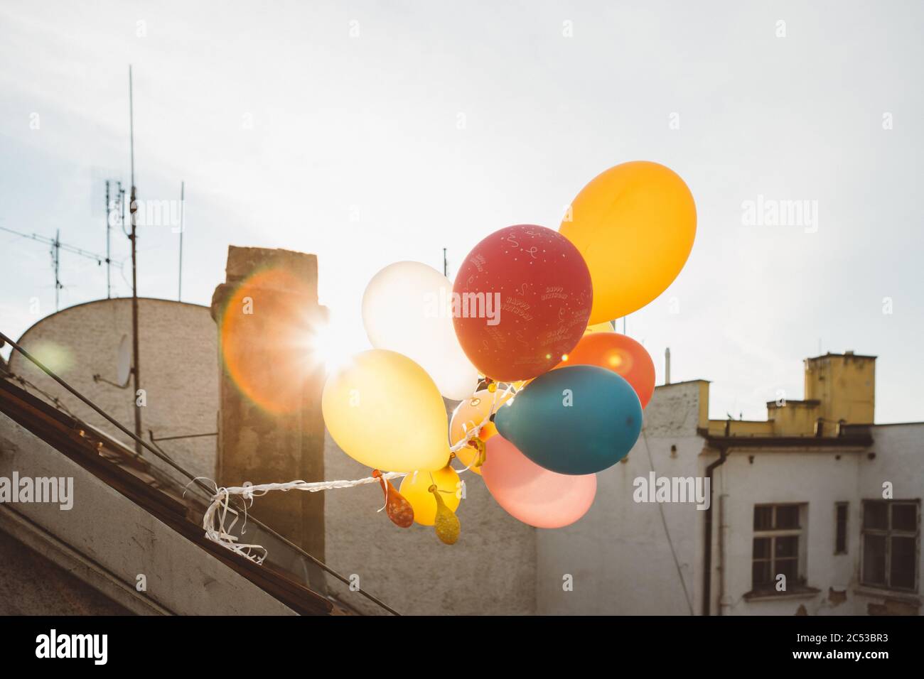 Colorati palloncini di compleanno, le decorazioni del tetto festa con il sole dietro durante il tramonto Foto Stock