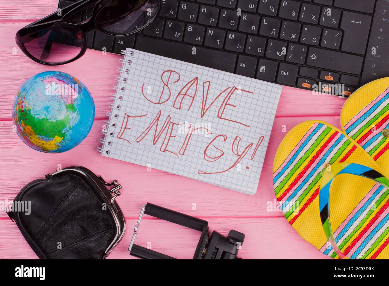Risparmia energia sul notebook con gli accessori da viaggio donna, il portafoglio con occhiali e infradito su sfondo rosa da tavolo. Foto Stock