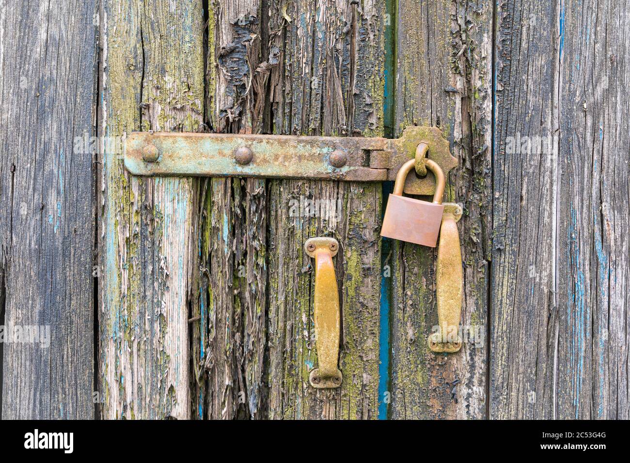 Primo piano di una vecchia porta in legno con vernice a scagliatura con lucchetto chiuso e vecchie maniglie. Foto Stock