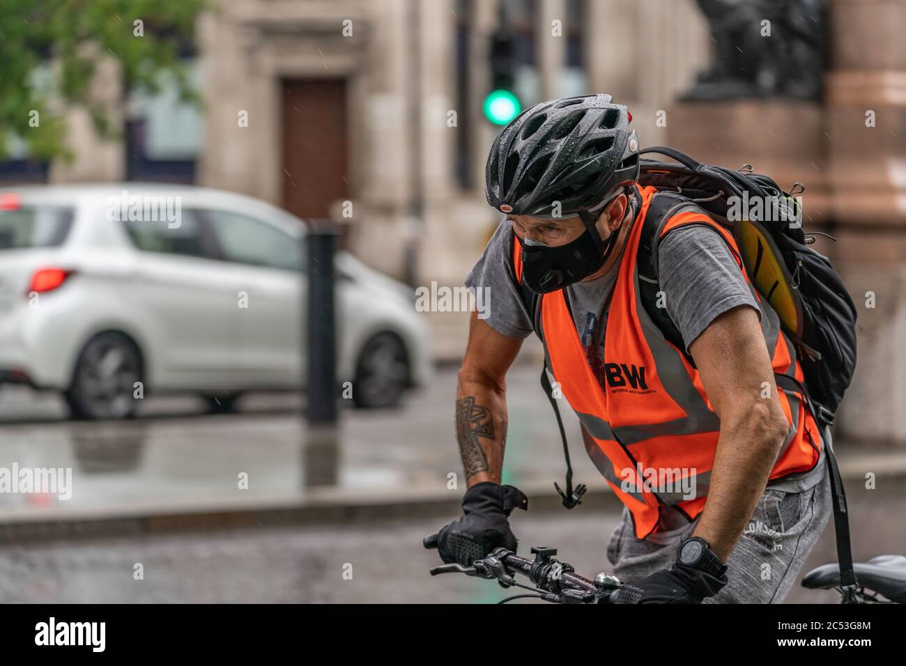 LONDRA, INGHILTERRA - 10 GIUGNO 2020: Ciclista giovane uomo che indossa una maschera facciale catturato fuori che lotta sotto la pioggia in una giornata frizzante a Holborn, Londra durante il giorno Foto Stock