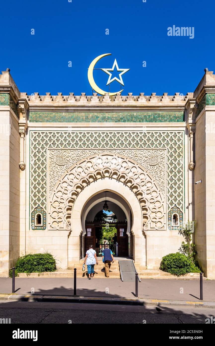 Vista frontale della facciata e della porta della Grande Moschea di Parigi, sormontata da una stella e una mezzaluna, contro il cielo blu. Foto Stock
